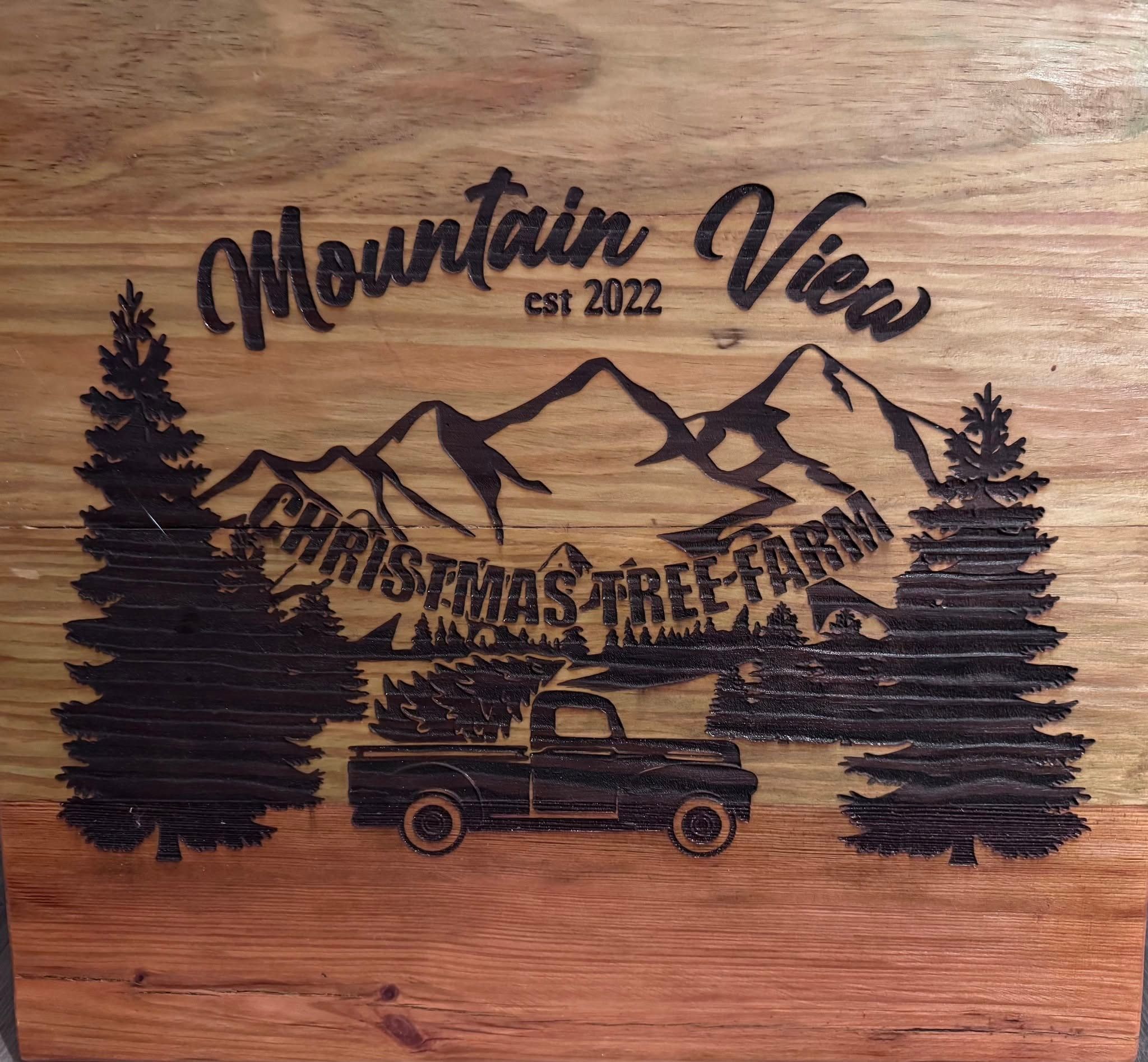 The Mountain View Christmas Tree Farm logo burned into a pine board: mountains, two fir trees and an old pickup hauling a tree.